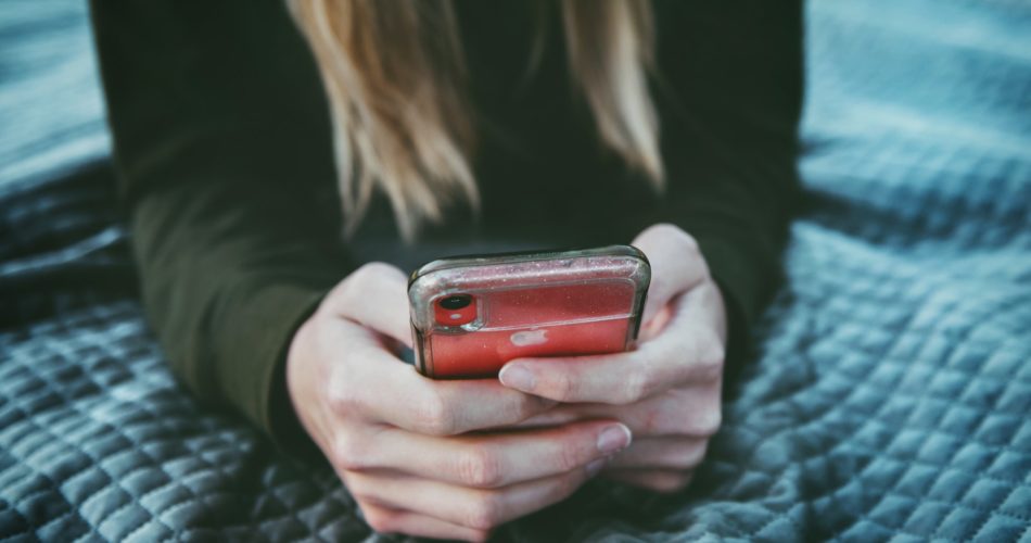 Une fille allongée dans son lit utilisant son téléphone pour chatter sur des sites de recontre gratuits